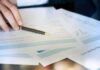 Hand with pen reviewing financial documents
