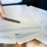 Hand with pen reviewing financial documents