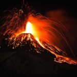 Volcano erupting at night with glowing lava and ash plume