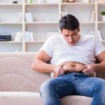 Men Pregnant? Planned Parenthood’s Claim Ignites Backlash Manny MUA sitting on a couch pinching his belly