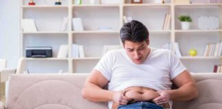 Manny MUA sitting on a couch pinching his belly