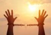 Knife-To-Throat Monster Up For Parole raised hands breaking chains against a sunset sky