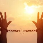 Knife-To-Throat Monster Up For Parole raised hands breaking chains against a sunset sky