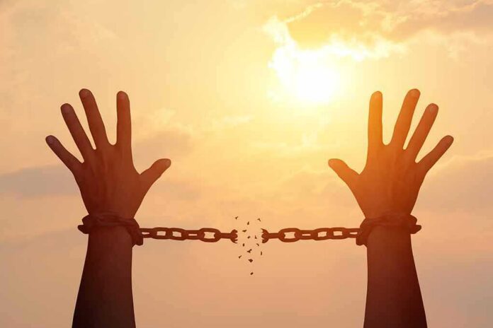 raised hands breaking chains against a sunset sky