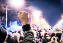 Albania’s Parliament Meltdown – Tear Gas Outside, Fists Inside Raised fist in front of a large crowd at night