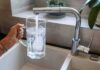 Abortion Pills In Tap? Testing Axed Hand holding a glass pitcher under a running kitchen faucet