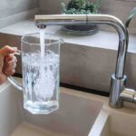 Abortion Pills In Tap? Testing Axed Hand holding a glass pitcher under a running kitchen faucet