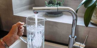 Hand holding a glass pitcher under a running kitchen faucet