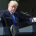Donald Trump speaking at dual podiums with arms outstretched