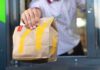 Did AI Quietly Sync McDonald’s Prices? Algorithmic Price Hike Panic Drive-thru worker handing a branded paper bag