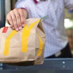 Did AI Quietly Sync McDonald’s Prices? Algorithmic Price Hike Panic Drive-thru worker handing a branded paper bag