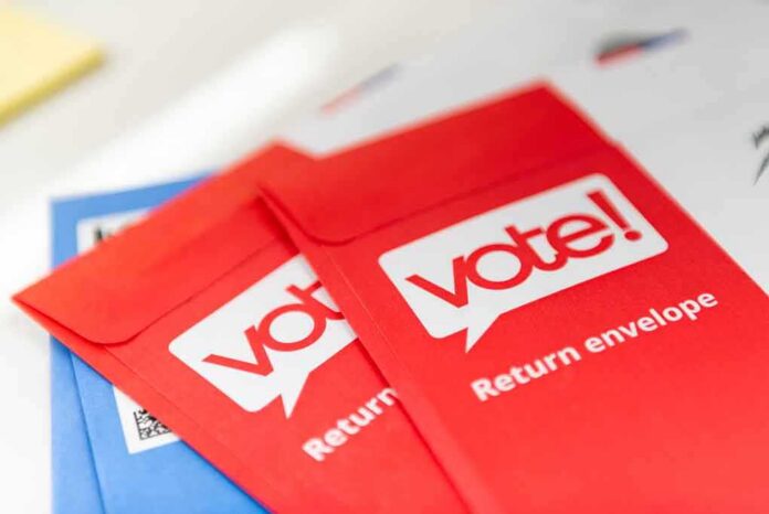 shutterstock_1671839164 Red vote return envelopes on a table