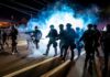 Riot police advance through tear gas at night on a city street