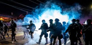 Riot police advance through tear gas at night on a city street
