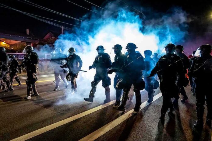 shutterstock_1794791068 Riot police advance through tear gas at night on a city street