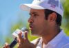 Man in white cap speaking into a microphone outdoors
