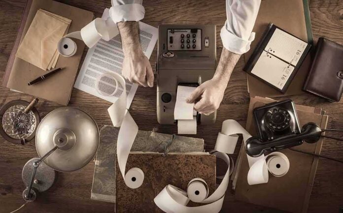 shutterstock_276522485 Accountant using vintage adding machine with paper tape