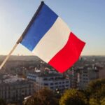France IGNITES: Looters Run Wild French flag waving over a city skyline at sunset